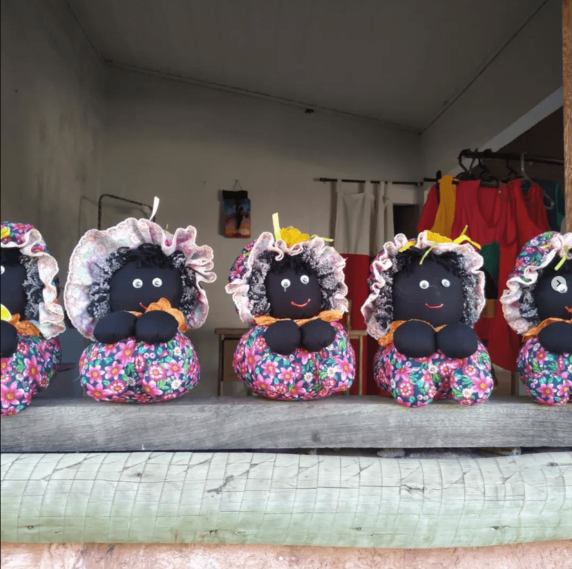 Pequenas bonecas artesanais negras dispostas lado a lado em uma janela.