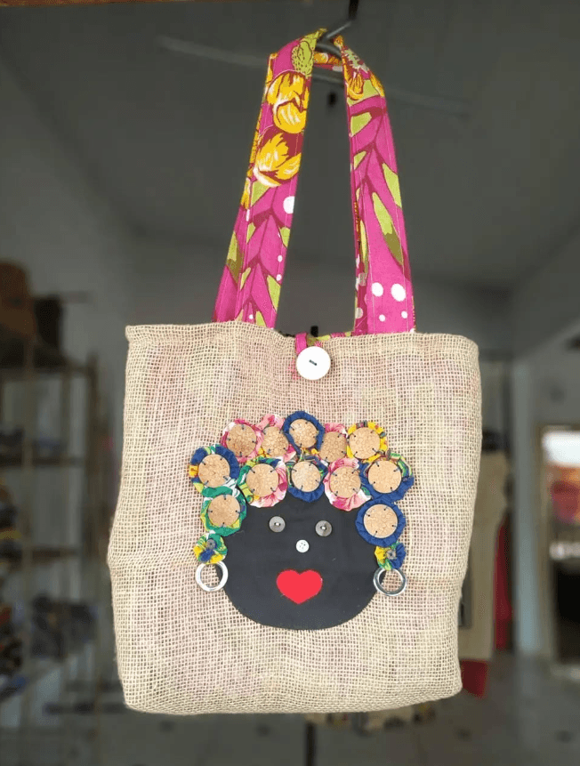 Bolsa artesanal de pano com o rosto de uma boneca negra na frente.